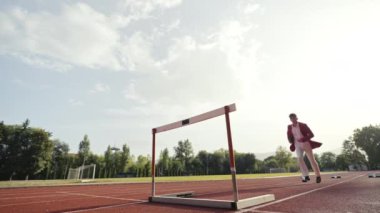 İş adamı atletizm pistinde koşarken engelden atlıyor. Yüksek kalite 4 bin yavaş çekim görüntüsü