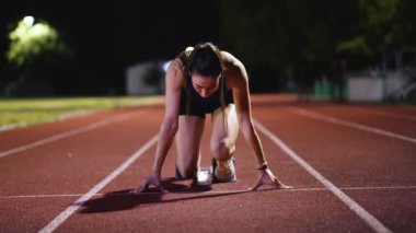 Atletizm atletizm sprint yarışı koşucusu koyu bir arka planda, stadyumun pistinde spor ayakkabılarla koşu koşusuna çıkıyor. Yavaş çekim