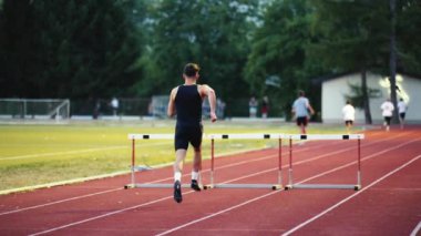 Güçlü Erkek Sporcu bir engele doğru koşuyor, bir yarışta koşarken bariyerin üzerinden yüksek hızda atlıyor. Hız Rampası Efektli Süper Yavaş Sinema Görüntüsü.