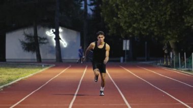 Güneşli bir sabahta atletizm pistinde koşan genç bir sporcunun dikey videosu. Spor anlayışı ve azim. Yüksek kalite 4k görüntü