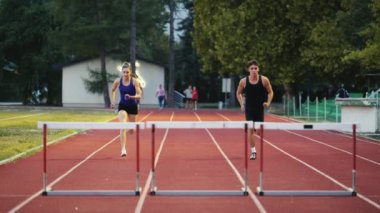 Stadyuma atletik zinde bir çift erkek ve kadın fırlatılıyor. Sıcak bir yaz öğleden sonrasında engellerin üzerinden atlamak. Yavaş Hareket İzleme Görüntüsü. 