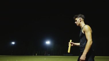 Erkek atlet, atletizm yarış pisti takım çalışması konseptinde bayrak yarışı sopasıyla oynuyor. Yüksek kalite ağır çekim 4k görüntü