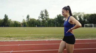 Atletizm pistinde maraton koştuktan sonra yorgun koşucu kadın nefes alıyor. Koşudan sonra nefes egzersizi yapan bir kız. Kadın dışarıda idmandan sonra dinleniyor. Yüksek kalite 4k görüntü
