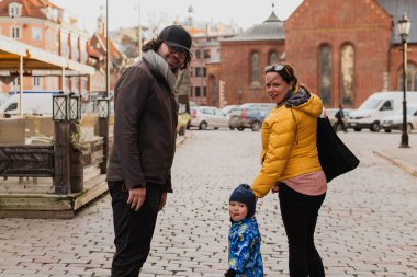 Parents walking hand in hand with their son through the charming city streets, enjoying the warmth of the season and creating joyful memories together clipart