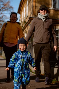 Sevgi dolu bir çift, sonbaharın canlı renkleriyle çevrili oğluyla birlikte güneşli bir parkta gezer. Neşeli ve huzurlu bir aile anının tadını çıkarırlar.