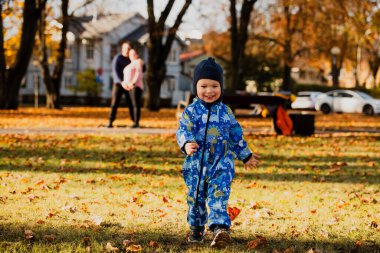 A joyful little boy in his winter coat and hat plays happily in the park, surrounded by the love and warmth of his smiling parents. clipart