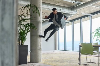 Modern bir ofise kendinden geçmiş bir şekilde atlayan bir işadamı, elinde bir evrak çantasıyla, başarı ve zafer anını kutluyor.