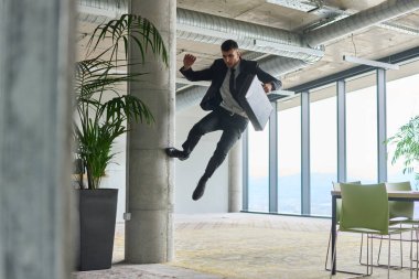 Modern bir ofise kendinden geçmiş bir şekilde atlayan bir işadamı, elinde bir evrak çantasıyla, başarı ve zafer anını kutluyor.