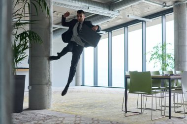 Modern bir ofise kendinden geçmiş bir şekilde atlayan bir işadamı, elinde bir evrak çantasıyla, başarı ve zafer anını kutluyor.