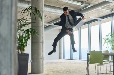 Modern bir ofise kendinden geçmiş bir şekilde atlayan bir işadamı, elinde bir evrak çantasıyla, başarı ve zafer anını kutluyor.