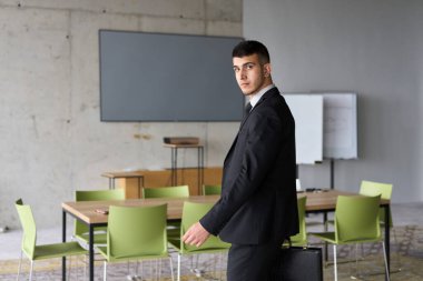 Siyah takım elbiseli kararlı bir işadamı ofisin içinde güven içinde yürüyor, profesyonelliği somutlaştırıyor ve yeni zorluklara doğru ilerlerken odaklanıyor.. 