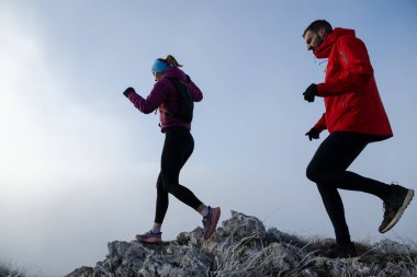 Sabahın erken saatlerinde dağın tepesinde koşan atlet çift patikası. Gökyüzü koşma konsepti, arka planda gökyüzü varken sınırda koşmak tehlikeli. Sağlıklı yaşam, kardiyo egzersizi, spor.