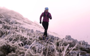 Koşan kadın sporcu, dağdaki ultra-maraton yarışına hazırlanıyor. Açık havada antrenman yapan koşucu bir kadın aktif ve zinde bir hayat sürüyor. Siluet sabahın erken saatlerinde.