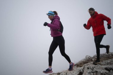 Sabahın erken saatlerinde dağın tepesinde koşan atlet çift patikası. Gökyüzü koşma konsepti, arka planda gökyüzü varken sınırda koşmak tehlikeli. Sağlıklı yaşam, kardiyo egzersizi, spor.