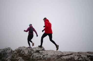 Sabahın erken saatlerinde dağın tepesinde koşan atlet çift patikası. Gökyüzü koşma konsepti, arka planda gökyüzü varken sınırda koşmak tehlikeli. Sağlıklı yaşam, kardiyo egzersizi, spor.