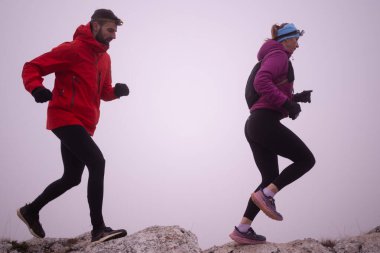 Sabahın erken saatlerinde dağın tepesinde koşan atlet çift patikası. Gökyüzü koşma konsepti, arka planda gökyüzü varken sınırda koşmak tehlikeli. Sağlıklı yaşam, kardiyo egzersizi, spor.