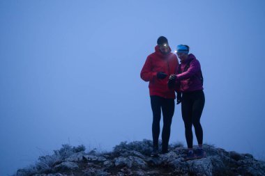 Eğitimden sonra nefes almaktan sıkılan koşucular, teknoloji sporu saatlerine bakmaktan, kalp atış hızı verilerini ve navigasyonlarını kontrol etmekten bıktılar. İki sporcu bir dağda birlikte koşuyor..