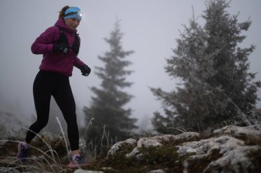 Bir dağda ultra-maraton koşusu için koşan bayan sporcu. Açık havada antrenman yapan koşucu bir kadın aktif ve zinde bir hayat sürüyor. Sabahın erken saatlerinde koşucular silueti.