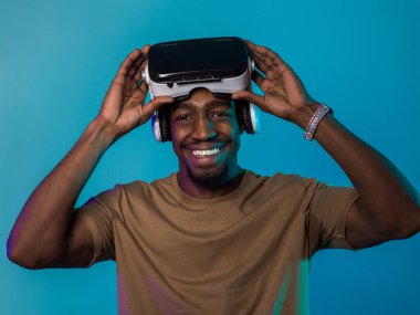 In a futuristic visual, an African American man stands isolated against a striking blue backdrop, adorned with VR glasses that transport him into a cutting-edge virtual reality experience, merging clipart