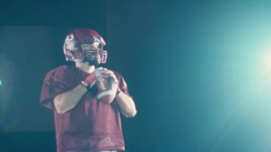 Sahada top atma ve yakalama pratiği yapan Amerikalı bir futbolcu, üniforma ve kask giyerek, dinamik hareketler ve kararlı bir atletik duruş ile becerilerini geliştirmeye odaklandı.