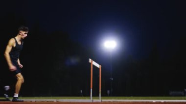 Güçlü Erkek Sporcu bir engele doğru koşuyor, bir yarışta koşarken bariyerin üzerinden yüksek hızda atlıyor. Hız Rampası Efektli Süper Yavaş Sinema Görüntüsü.