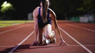 Atletizm atletizm sprint yarışı koşucusu koyu bir arka planda, stadyumun pistinde spor ayakkabılarla koşu koşusuna çıkıyor. Yavaş çekim