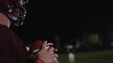Sahada top atma ve yakalama pratiği yapan Amerikalı bir futbolcu, üniforma ve kask giyerek, dinamik hareketler ve kararlı bir atletik duruş ile becerilerini geliştirmeye odaklandı.