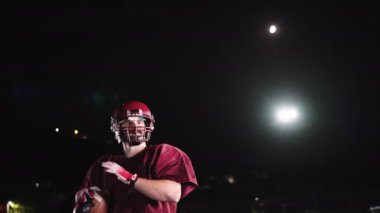 Sahada top atma ve yakalama pratiği yapan Amerikalı bir futbolcu, üniforma ve kask giyerek, dinamik hareketler ve kararlı bir atletik duruş ile becerilerini geliştirmeye odaklandı.