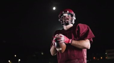 Sahada top atma ve yakalama pratiği yapan Amerikalı bir futbolcu, üniforma ve kask giyerek, dinamik hareketler ve kararlı bir atletik duruş ile becerilerini geliştirmeye odaklandı.