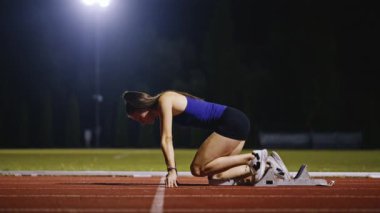 Atletizm atletizm sprint yarışı koşucusu koyu bir arka planda, stadyumun pistinde spor ayakkabılarla koşu koşusuna çıkıyor. Yavaş çekim