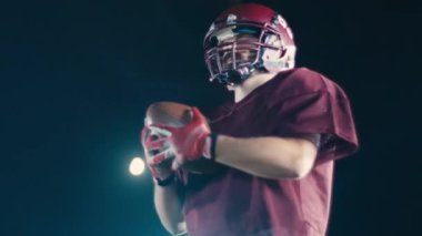 Sahada top atma ve yakalama pratiği yapan Amerikalı bir futbolcu, üniforma ve kask giyerek, dinamik hareketler ve kararlı bir atletik duruş ile becerilerini geliştirmeye odaklandı.