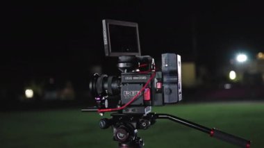 Bir film setinde, kablolarla, monitörlerle ve ışıklandırma ekipmanlarıyla çevrili bir tripoda ya da platforma monte edilmiş yüksek çözünürlüklü film yapımına hazır bir RED Dijital Kamera.