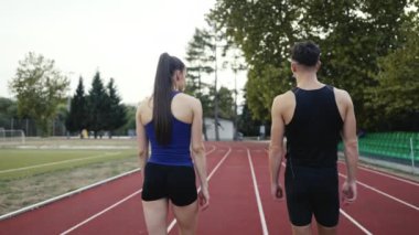 Sportif atletizm çifti stadyumun etrafında koşmayı bitirdi. Spor pistinde dinlenirken yürüyorlar ve keyifli sohbetler ederken nefes alıyorlar. Yüksek kalite 4 bin ağır çekim