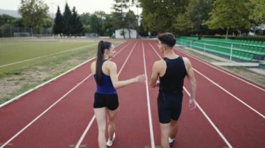 Sportif atletizm çifti stadyumun etrafında koşmayı bitirdi. Spor pistinde dinlenirken yürüyorlar ve keyifli sohbetler ederken nefes alıyorlar. Yüksek kalite 4 bin ağır çekim