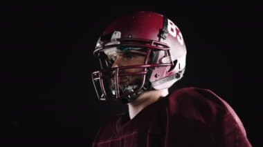 Stadyum ışıkları altında yoğun gece eğitimi sırasında çekilen tam teçhizatlı bir Amerikan futbolcusunun dinamik portresi.