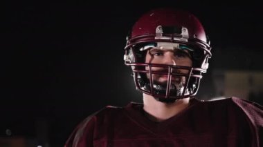 Stadyum ışıkları altında yoğun gece eğitimi sırasında çekilen tam teçhizatlı bir Amerikan futbolcusunun dinamik portresi.