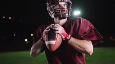 Sahada top atma ve yakalama pratiği yapan Amerikalı bir futbolcu, üniforma ve kask giyerek, dinamik hareketler ve kararlı bir atletik duruş ile becerilerini geliştirmeye odaklandı.