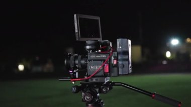 Bir film setinde, kablolarla, monitörlerle ve ışıklandırma ekipmanlarıyla çevrili bir tripoda ya da platforma monte edilmiş yüksek çözünürlüklü film yapımına hazır bir RED Dijital Kamera.