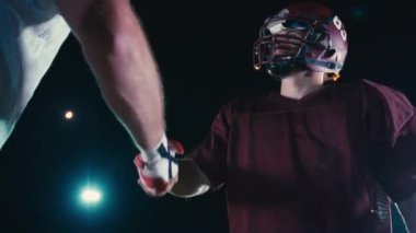 Amerikan futbolcularının el sıkışması, takım çalışmasının, sportmenliğin ve stadyum ışıkları altında arkadaşlığın kutlanması için samimi bir an.