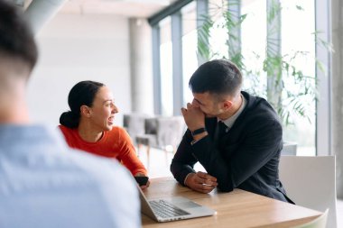 Genç, çeşitli bir iş ekibi modern bir ofiste birlikte oturuyor, fikir ve iş planlarını paylaşıyor, gelecekteki başarı için işbirliği ve yenilikleri teşvik ediyor.