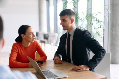 Genç, çeşitli bir iş ekibi modern bir ofiste birlikte oturuyor, fikir ve iş planlarını paylaşıyor, gelecekteki başarı için işbirliği ve yenilikleri teşvik ediyor.