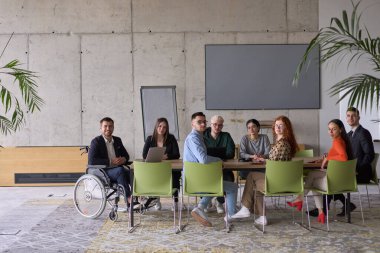 Muhtelif bir grup iş adamı, yöneticileriyle bir ofiste oturuyorlar, şu anda tekerlekli sandalyede, işbirliği, liderlik ve kapsayıcılığı destekliyorlar..