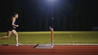 Dişi sporcu bir engele doğru koşuyor, engelli koşuyor, yüksek hızda bariyerin üzerinden atlıyor bir yarışta koşarken. Hız Rampası Efektli Süper Yavaş Sinema Görüntüsü.