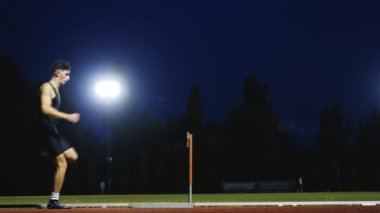 Güçlü Erkek Sporcu bir engele doğru koşuyor, bir yarışta koşarken bariyerin üzerinden yüksek hızda atlıyor. Hız Rampası Efektli Süper Yavaş Sinema Görüntüsü.