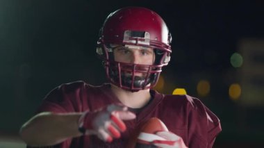 Profesyonel Amerikan futbolcusunun portresi miğferli, dramatik bir ışık altında maça hazır kusuyor. Takım oyunu ve ekstrem spor ruhu iş dünyası liderliği kavramı. Sinema yavaşlığı