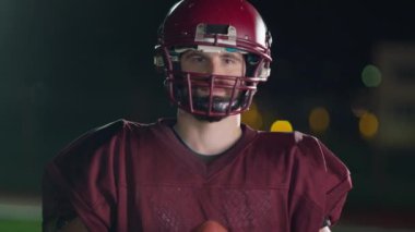 Profesyonel Amerikan futbolcusunun portresi miğferli, dramatik bir ışık altında maça hazır kusuyor. Takım oyunu ve ekstrem spor ruhu iş dünyası liderliği kavramı. Sinema yavaşlığı