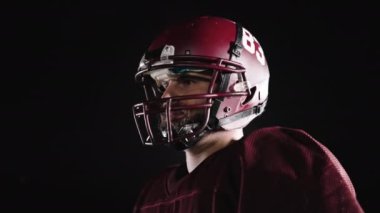 Stadyum ışıkları altında yoğun gece eğitimi sırasında çekilen tam teçhizatlı bir Amerikan futbolcusunun dinamik portresi.