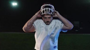 Bir stadyumda kameraya bakan beyaz bir Amerikan futbolcusunun profesyonel portresi. Odaklanmış ve kararlı bir şekilde kaskını takıyor ve başarılı bir şampiyonluk maçına hazırlanıyor.