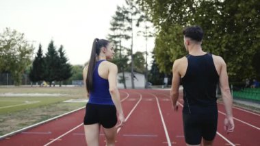 Sportif atletizm çifti stadyumun etrafında koşmayı bitirdi. Spor pistinde dinlenirken yürüyorlar ve keyifli sohbetler ederken nefes alıyorlar. Yüksek kalite 4 bin ağır çekim