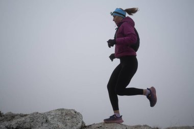 Gökyüzü koşuyor ya da bir dağın tepesinde egzersiz yapan bir kadını takip ediyor. Açık havada antrenman yapan koşucu bir kadın aktif ve zinde bir hayat sürüyor. Siluet sabahın erken saatlerinde.